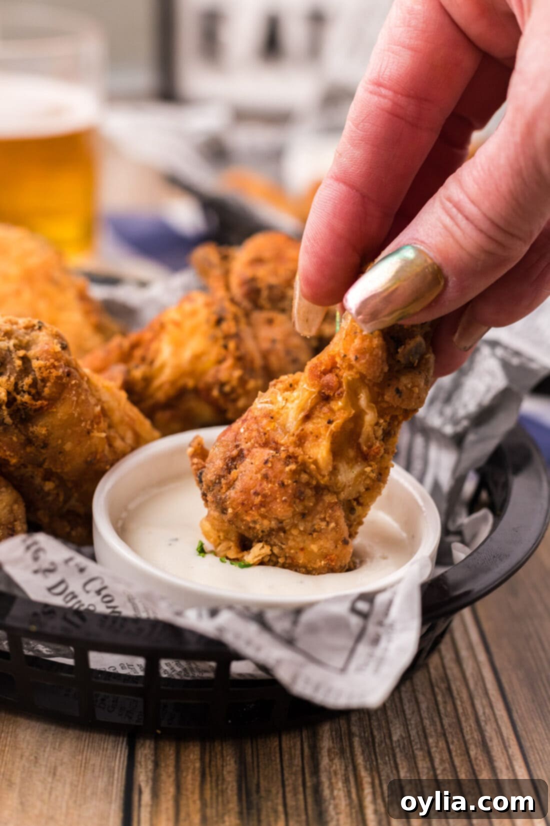 A golden-brown fried chicken wing being dipped into a small bowl of creamy ranch dressing, highlighting its crispy texture.