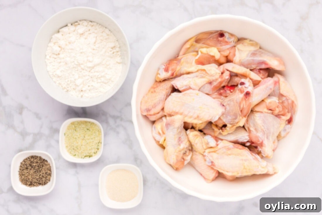 A selection of fresh ingredients laid out on a wooden board, including raw chicken wings, a bowl of all-purpose flour, garlic salt, black pepper, and onion powder, ready for making fried chicken wings.