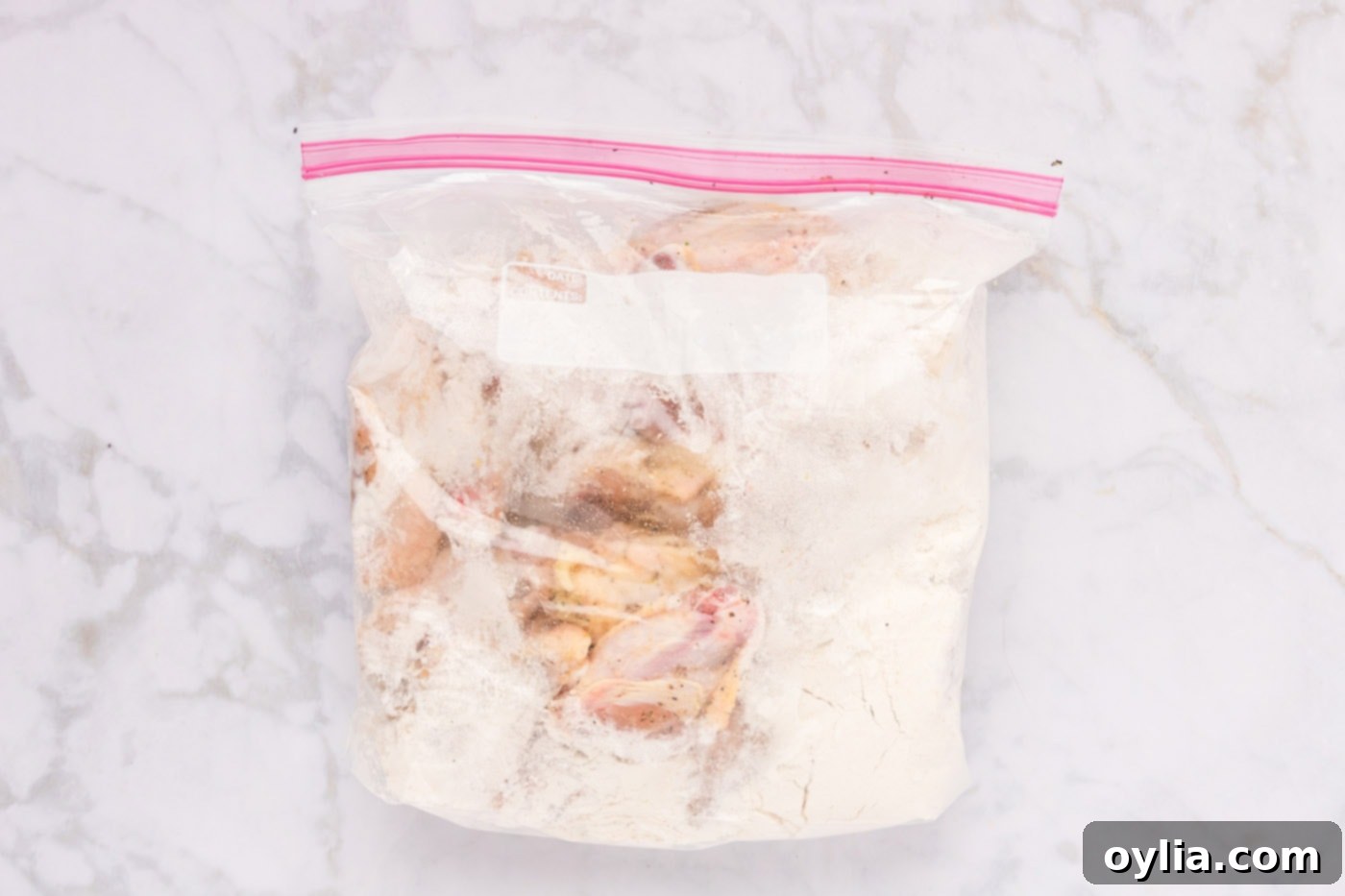 Raw chicken wings covered in a white flour mixture inside a clear plastic zip-top bag, showing even coating.