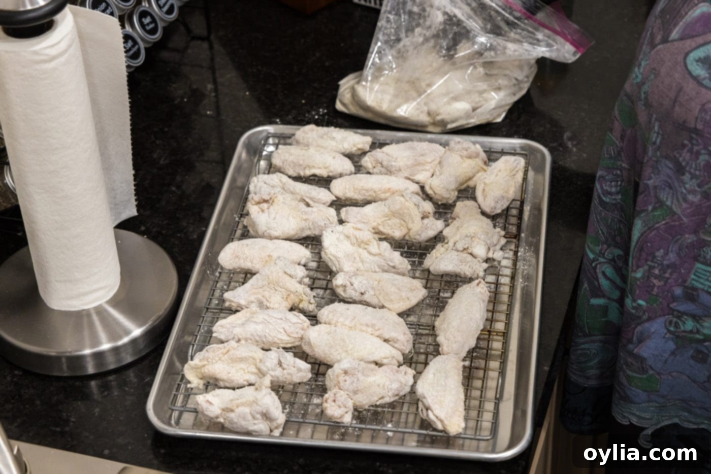 Floured chicken wings resting on a wire rack set over a baking sheet, with a light coating of seasoned flour.