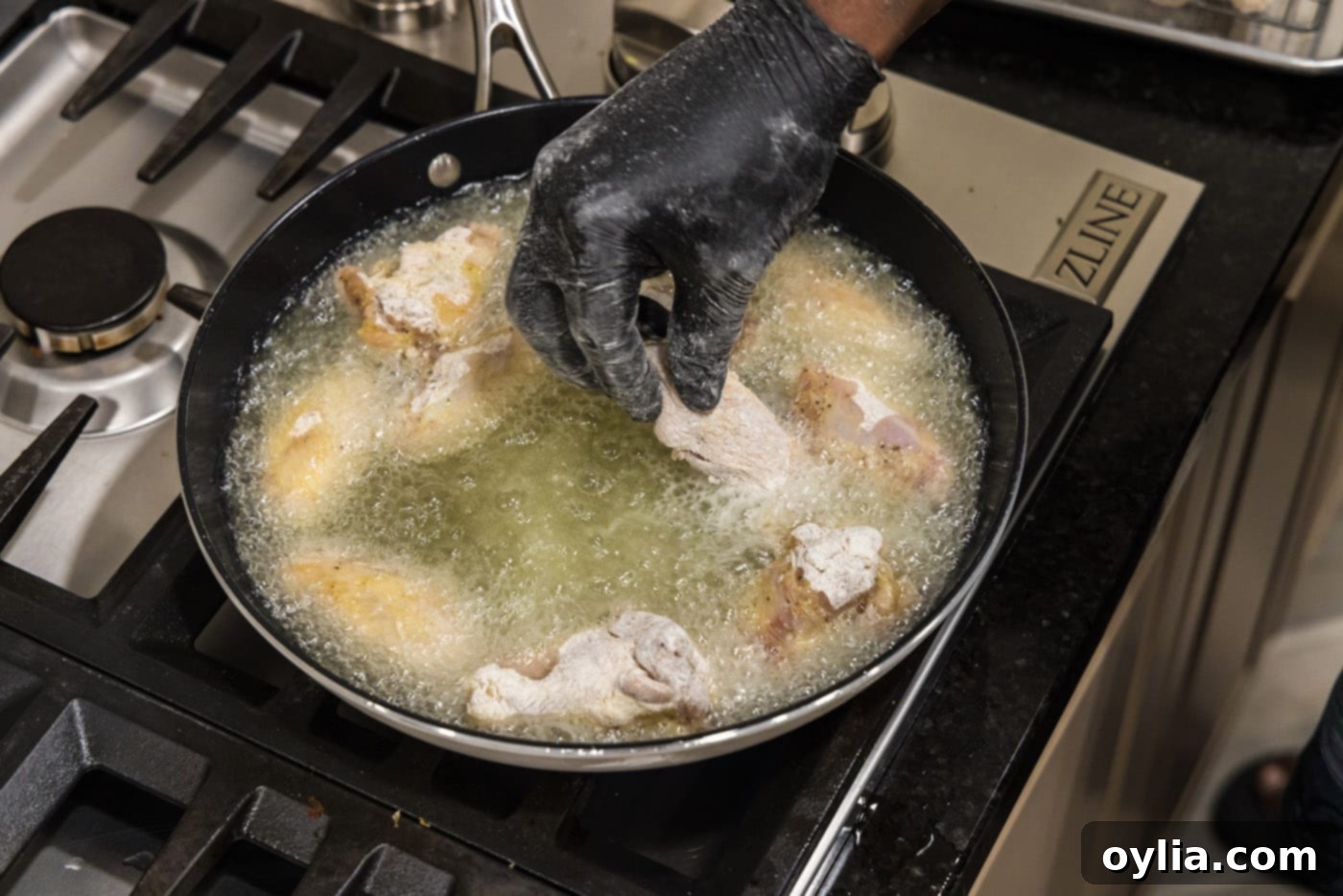 Several floured chicken wings carefully placed into a large skillet with hot, shimmering oil, ready for frying.