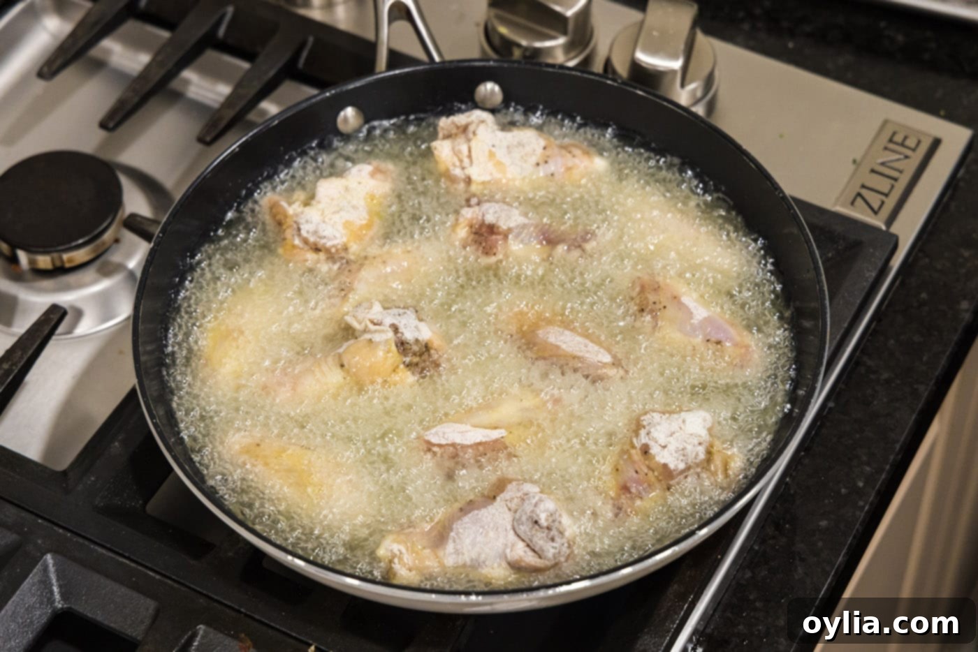 Chicken wings sizzling and frying in hot oil in a skillet, turning golden brown as they cook.
