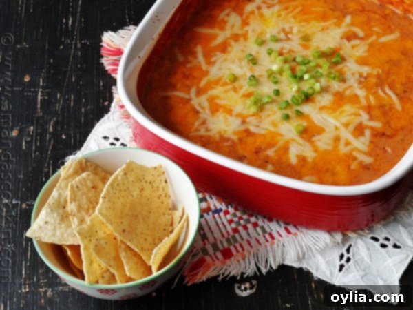 Creamy con queso bean dip in a red bowl with tortilla chips on the side, ready for serving.