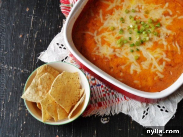 Overhead view of creamy con queso bean dip in a red dish, perfectly complemented by golden tortilla chips.