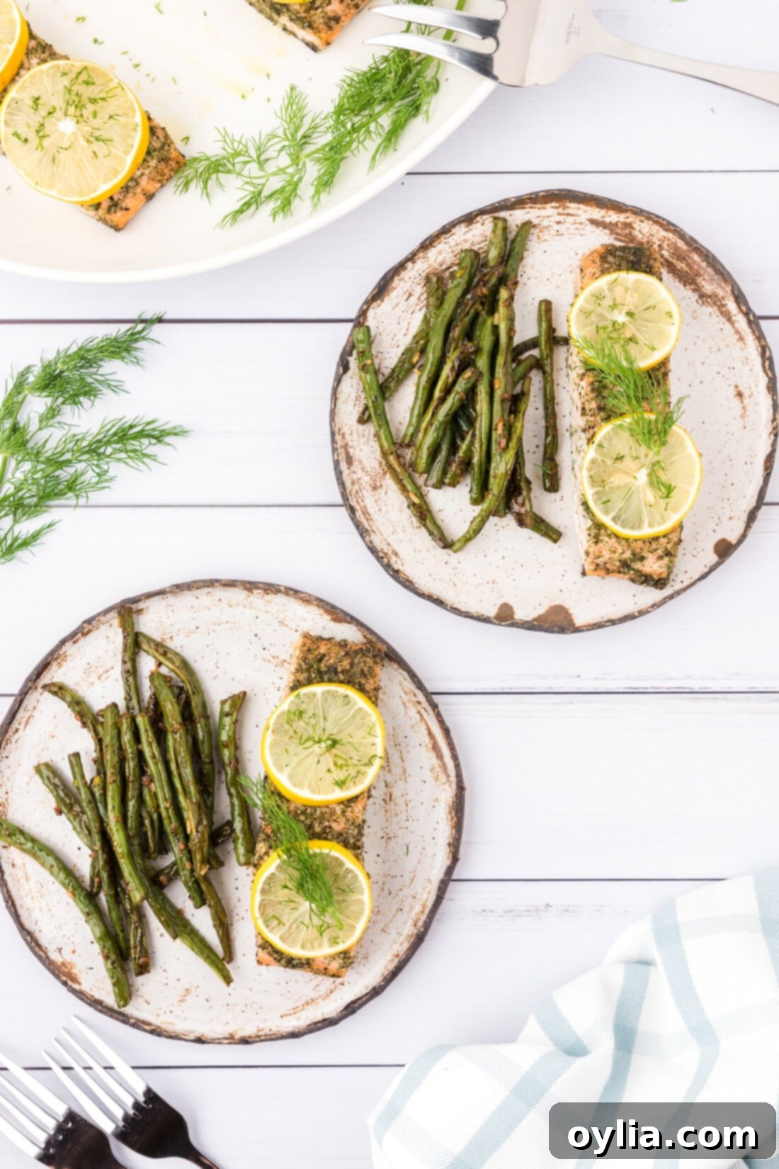 Two plates of beautifully baked dill salmon with lemon slices and a side of vibrant green beans, ready to be served for a healthy and quick dinner.