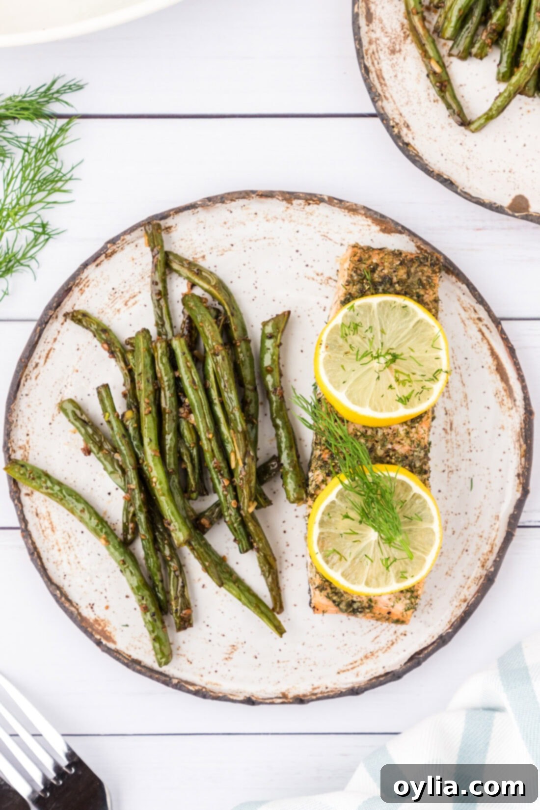 A single serving of baked dill salmon with lemon slices, perfectly flaky, served on a white plate with a generous portion of roasted green beans.