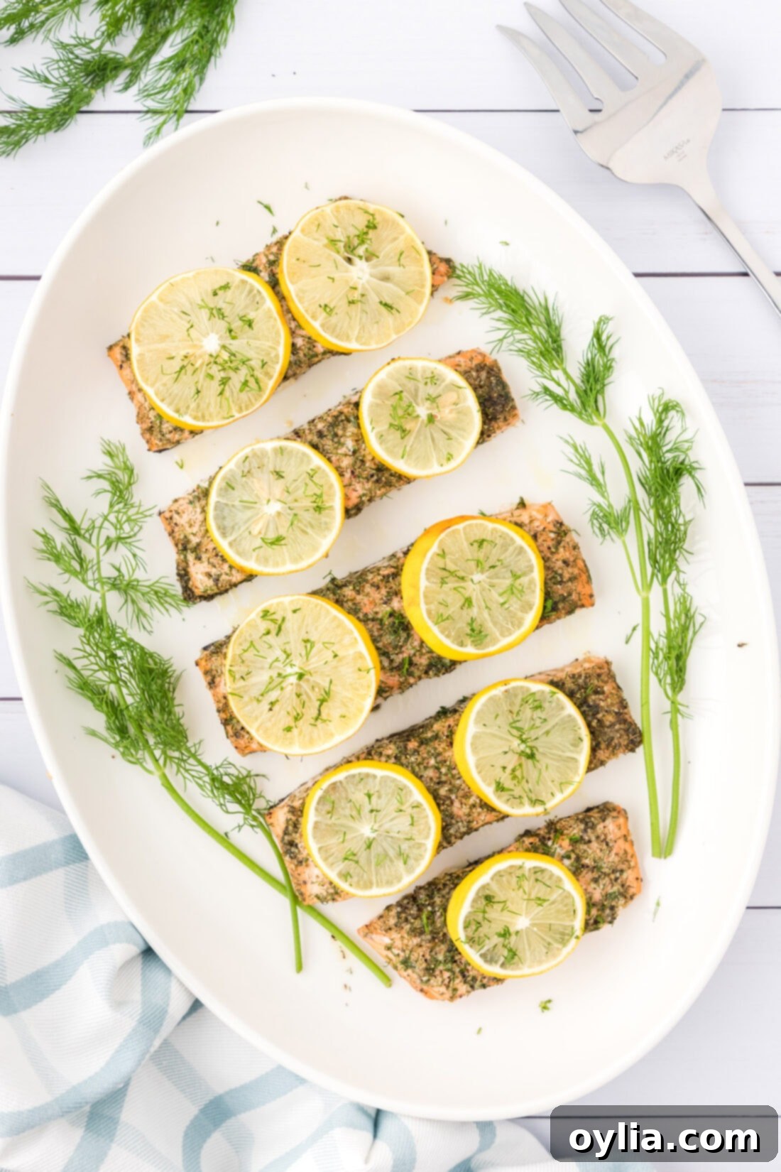 A large platter showcasing several perfectly baked dill salmon fillets, garnished with fresh lemon slices and a sprinkle of fresh dill, ready for serving.