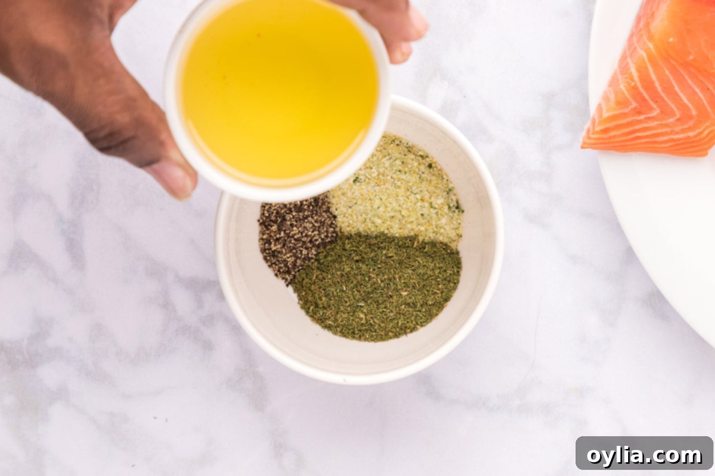 Pouring olive oil over a bowl filled with dried dill, garlic salt, and black pepper for the salmon seasoning.