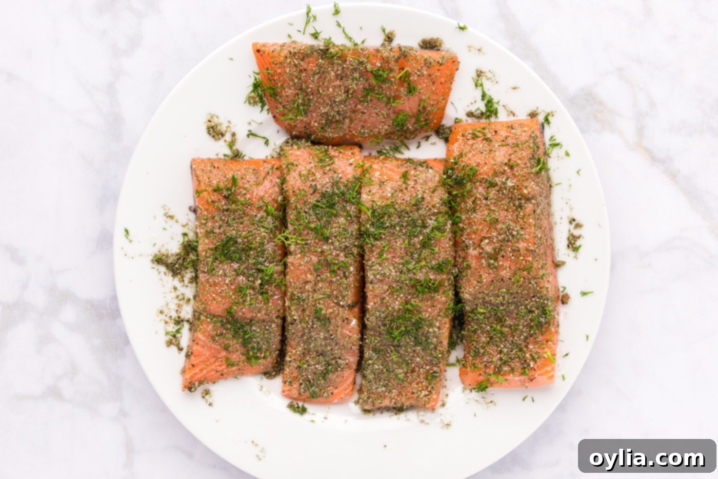 Salmon fillets coated in a savory dill rub, with fresh dill sprigs already placed on top, ready for baking.