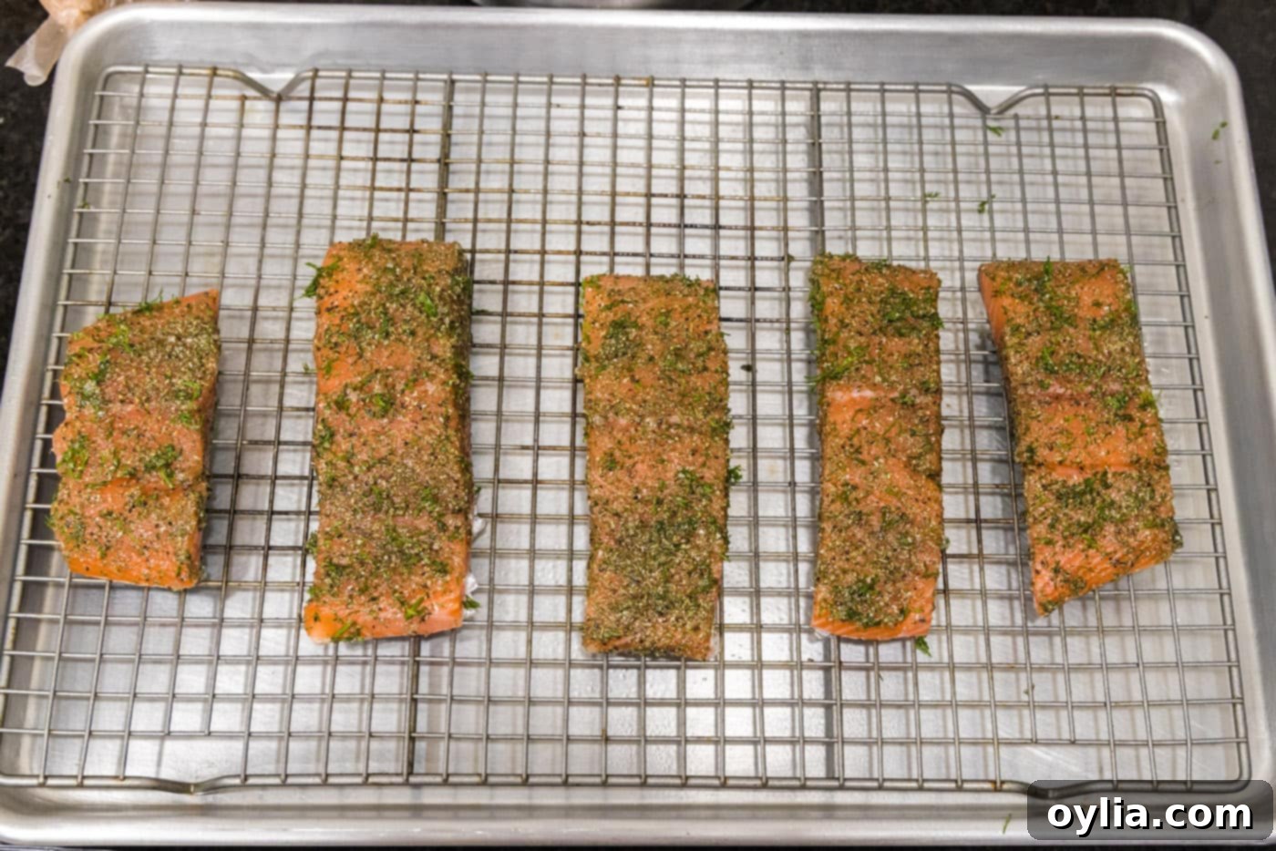 Dill salmon fillets meticulously arranged on a wire rack over a baking sheet, prepped for the oven.