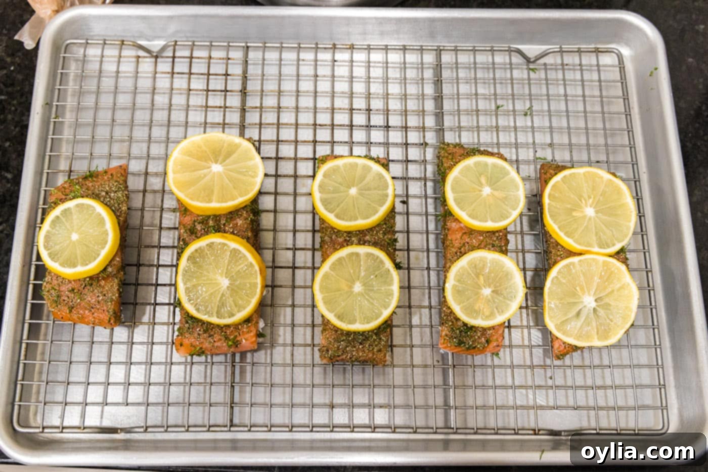 Fresh lemon slices delicately placed on top of dill salmon fillets on the baking sheet.