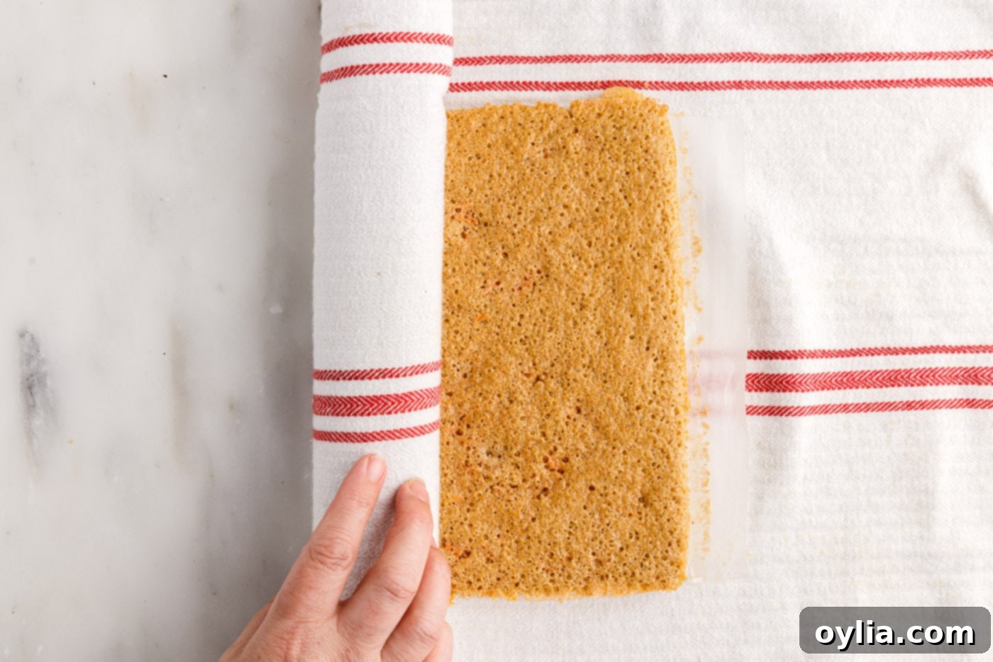 Carrot cake being carefully rolled into a log with a tea towel, to set its shape during cooling