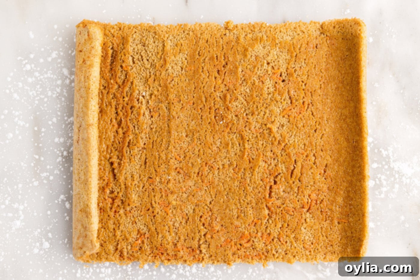 The carrot cake roll fully unrolled onto a powdered sugar-dusted surface, flat and ready for filling