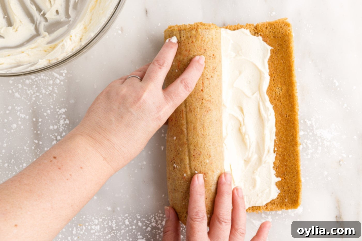 The carrot cake being re-rolled with the cream cheese filling inside, creating the spiral