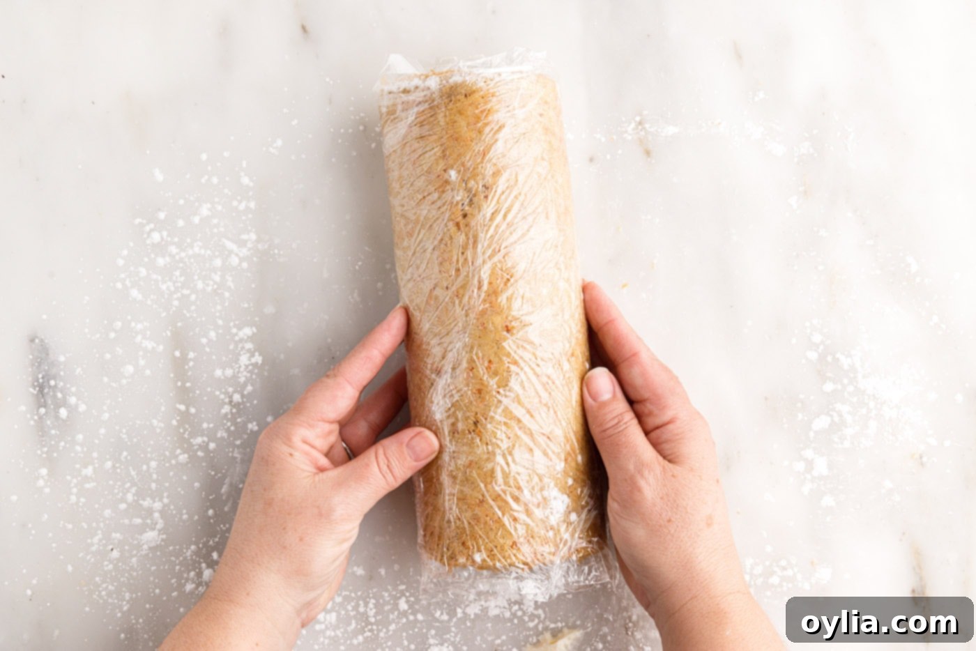 The carrot cake roll tightly wrapped in plastic wrap, ready for chilling to set its shape