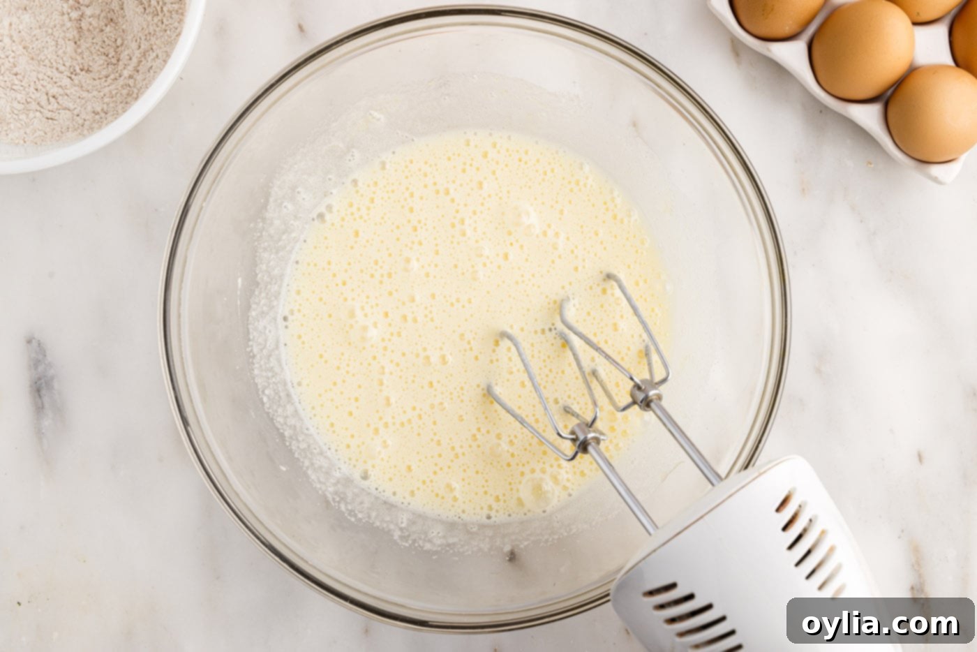 Eggs and sugar being whisked together in a bowl until foamy and pale with an electric mixer