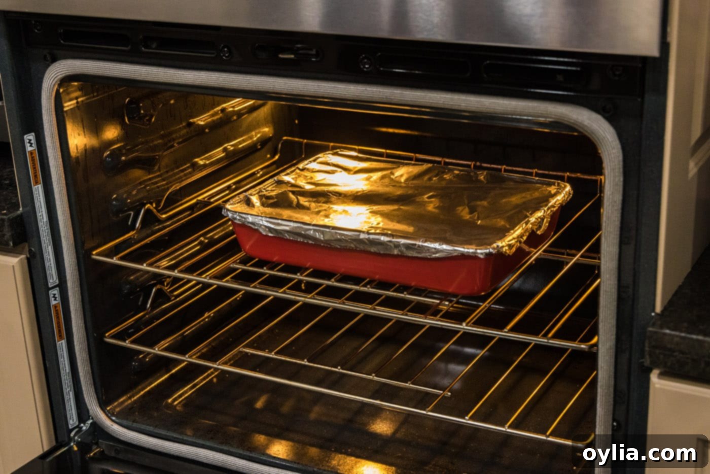 Boneless beef short ribs baking in the oven, covered with aluminum foil, undergoing the slow braising process.