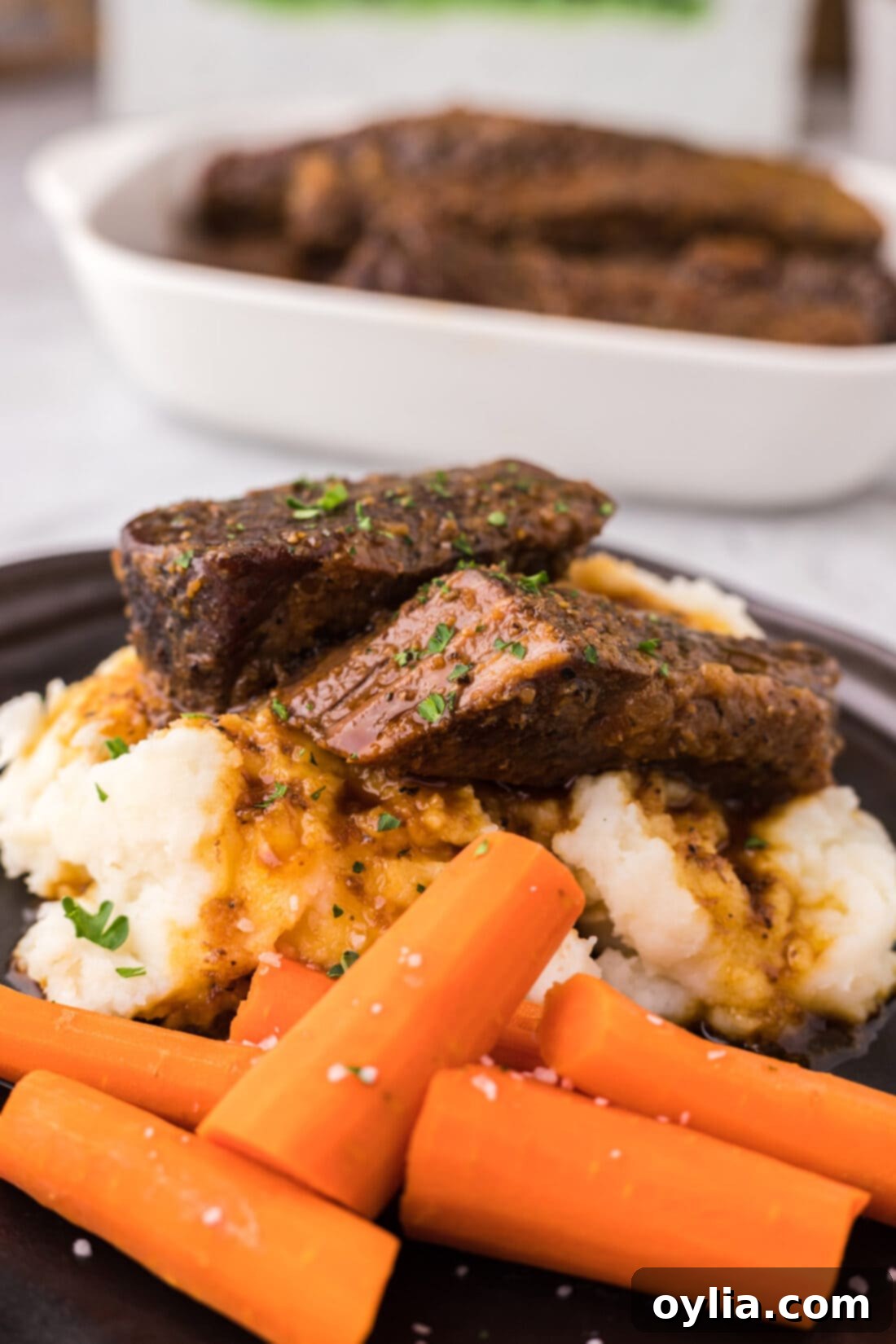A hearty plate of boneless beef short ribs served on a bed of mashed potatoes, accompanied by roasted carrots, ready to be devoured.