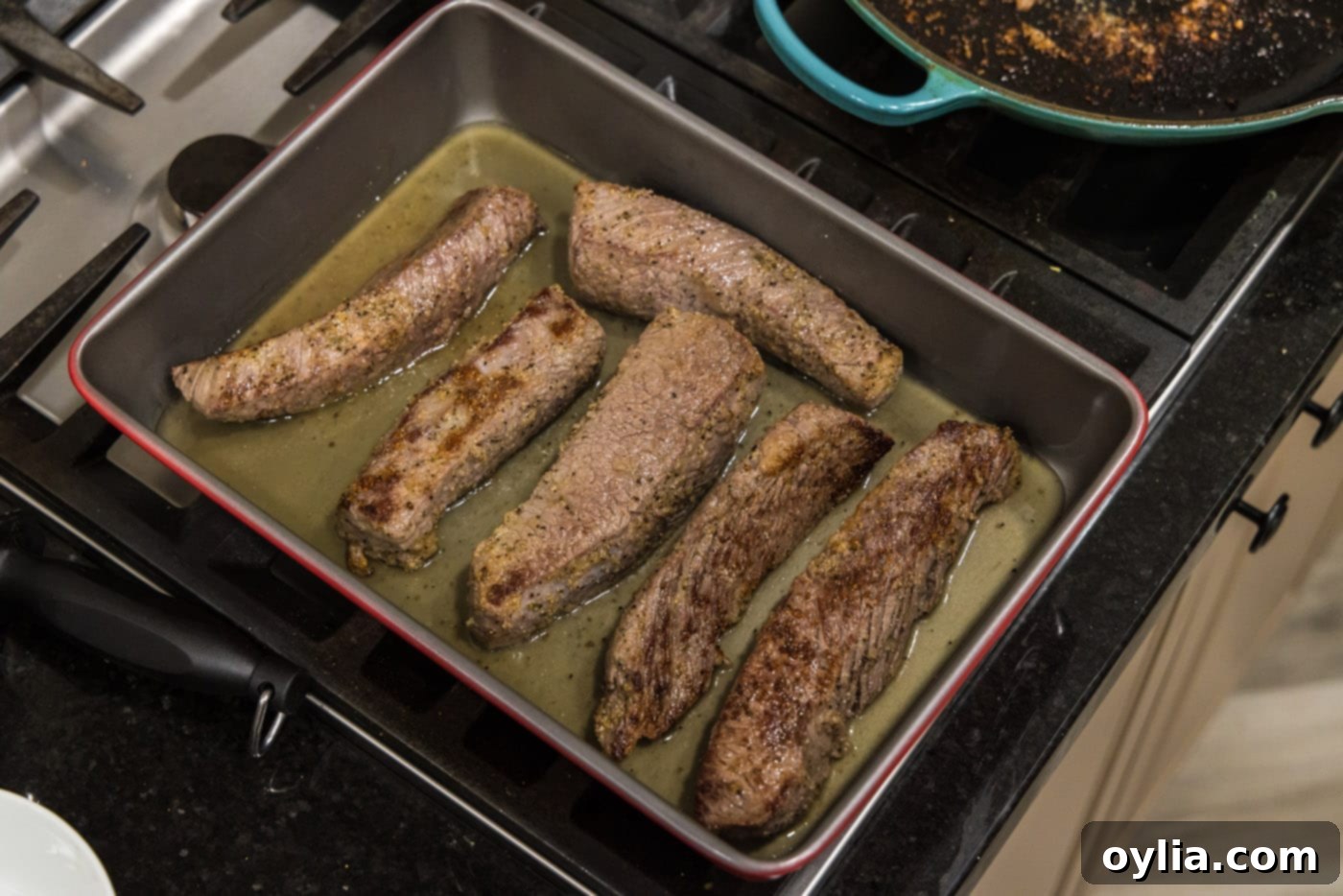 Boneless beef short ribs arranged in a baking dish with chicken broth at the bottom.