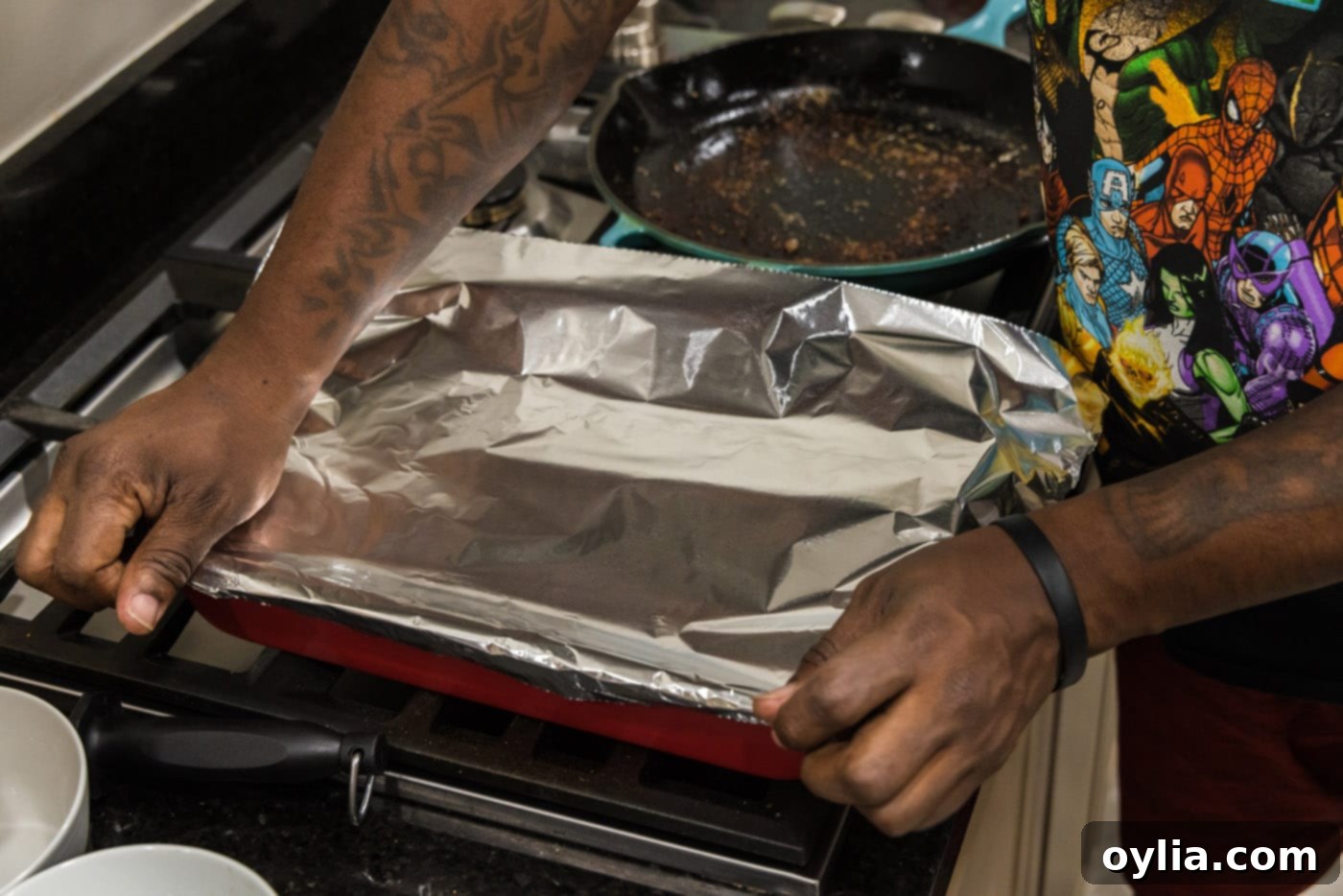 Covering the baking pan filled with beef short ribs and broth tightly with aluminum foil for oven braising.