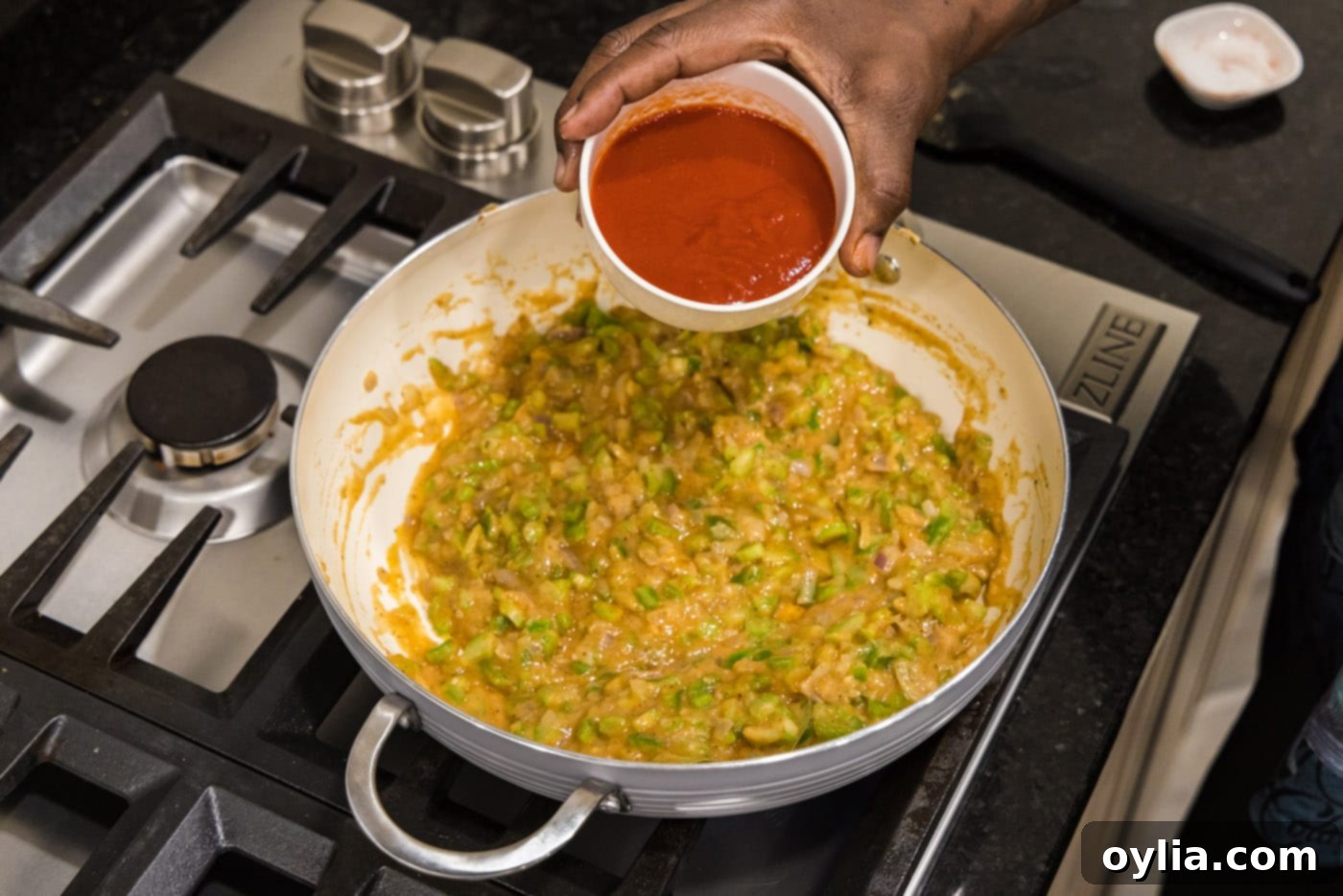 pouring tomato sauce into skillet with vegetable roux for a rich Creole etouffee
