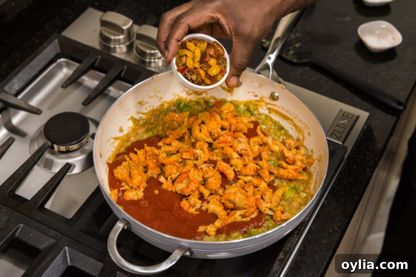 adding cherry tomatoes to crawfish etouffee in a skillet for freshness and color