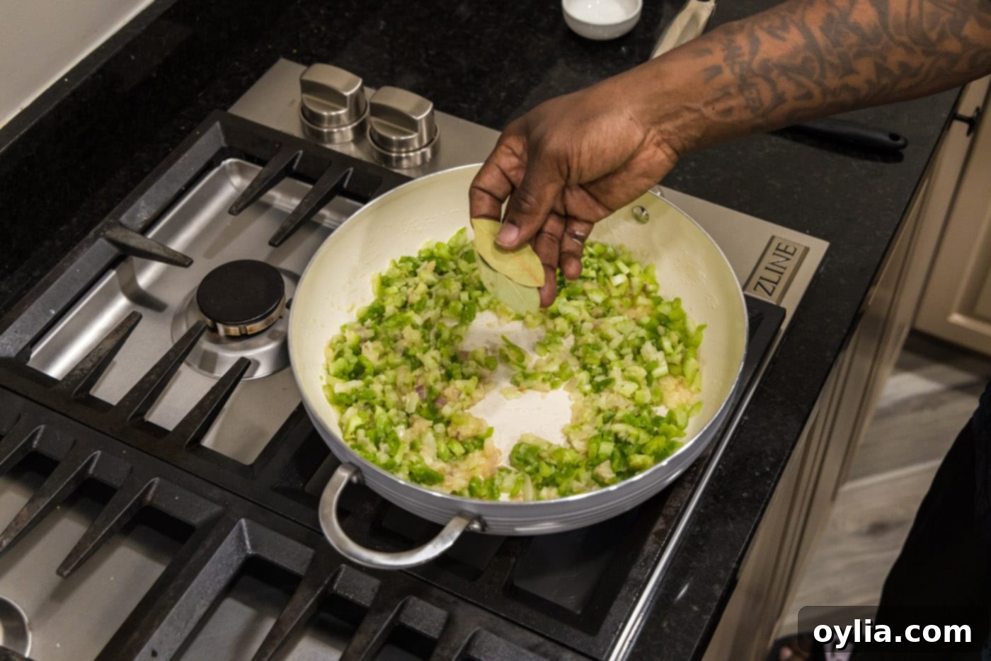 adding bay leaves to skillet of onion, bell pepper, and celery for aromatic depth