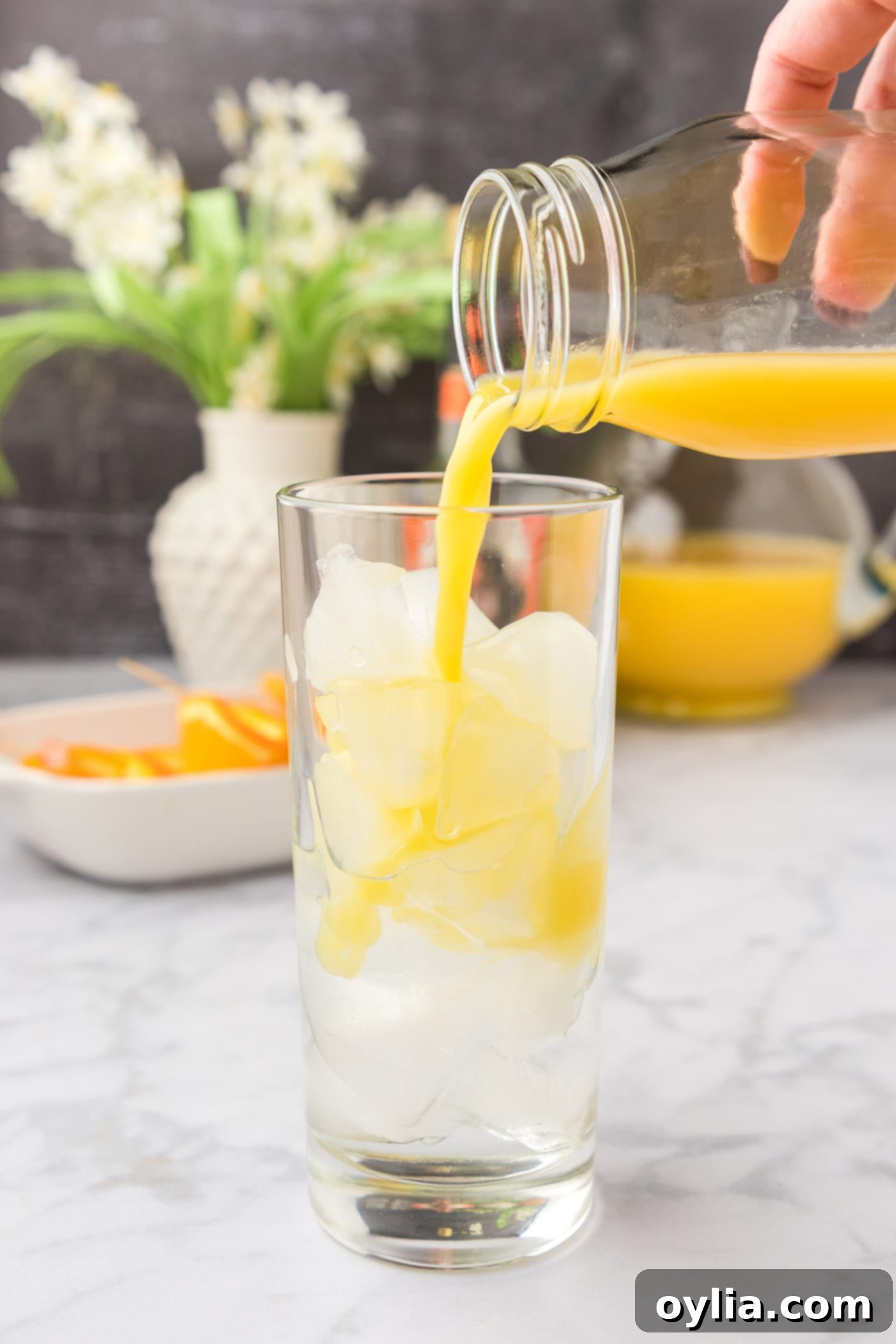 pouring orange juice into glass of peach schnapps and ice