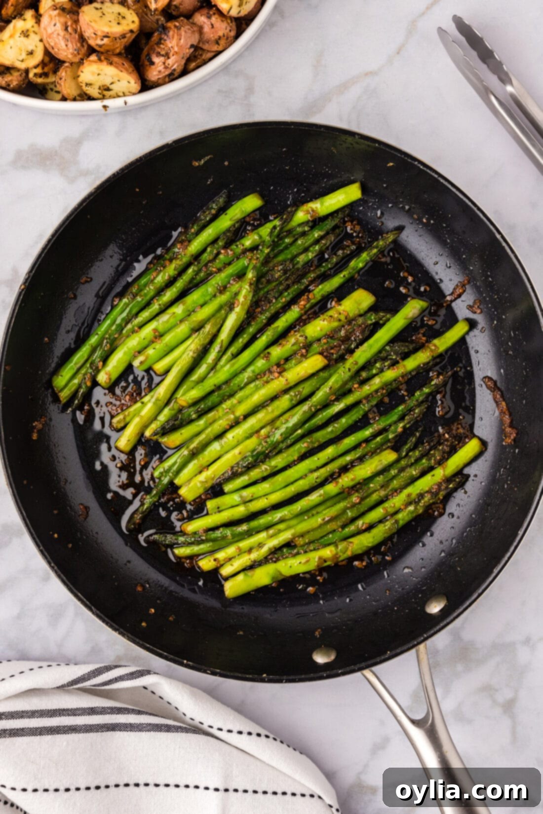 Sautéed Asparagus presented in a skillet, with a side of golden roasted red potatoes blurred in the background, creating a complete meal visual.