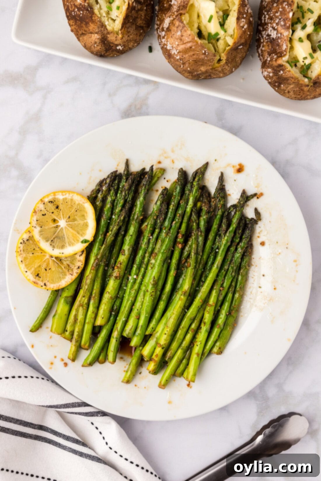 Sautéed Asparagus arranged on a white plate with fresh lemon slices, ready to serve.