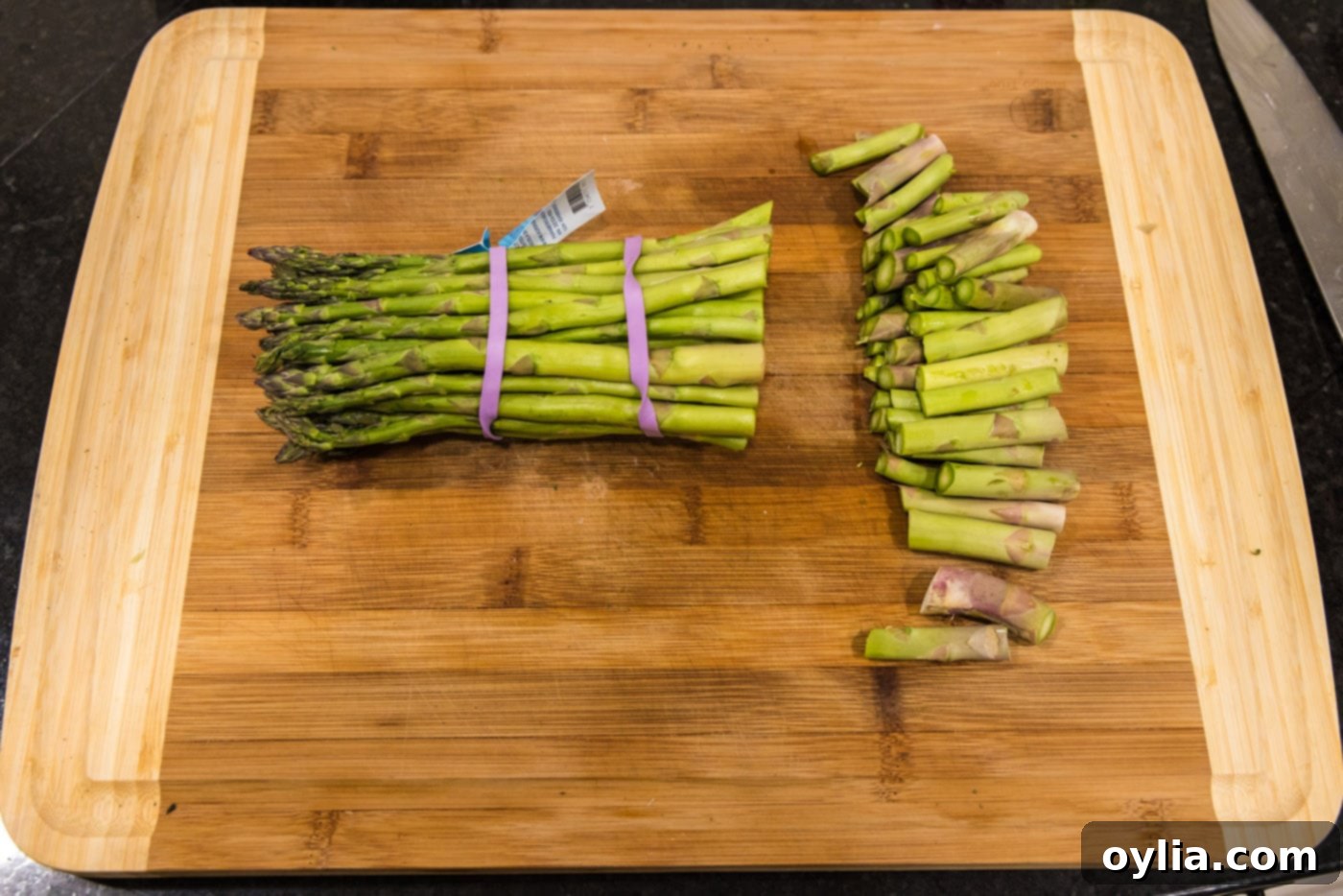 A hand demonstrating how to trim the woody ends off fresh asparagus spears.
