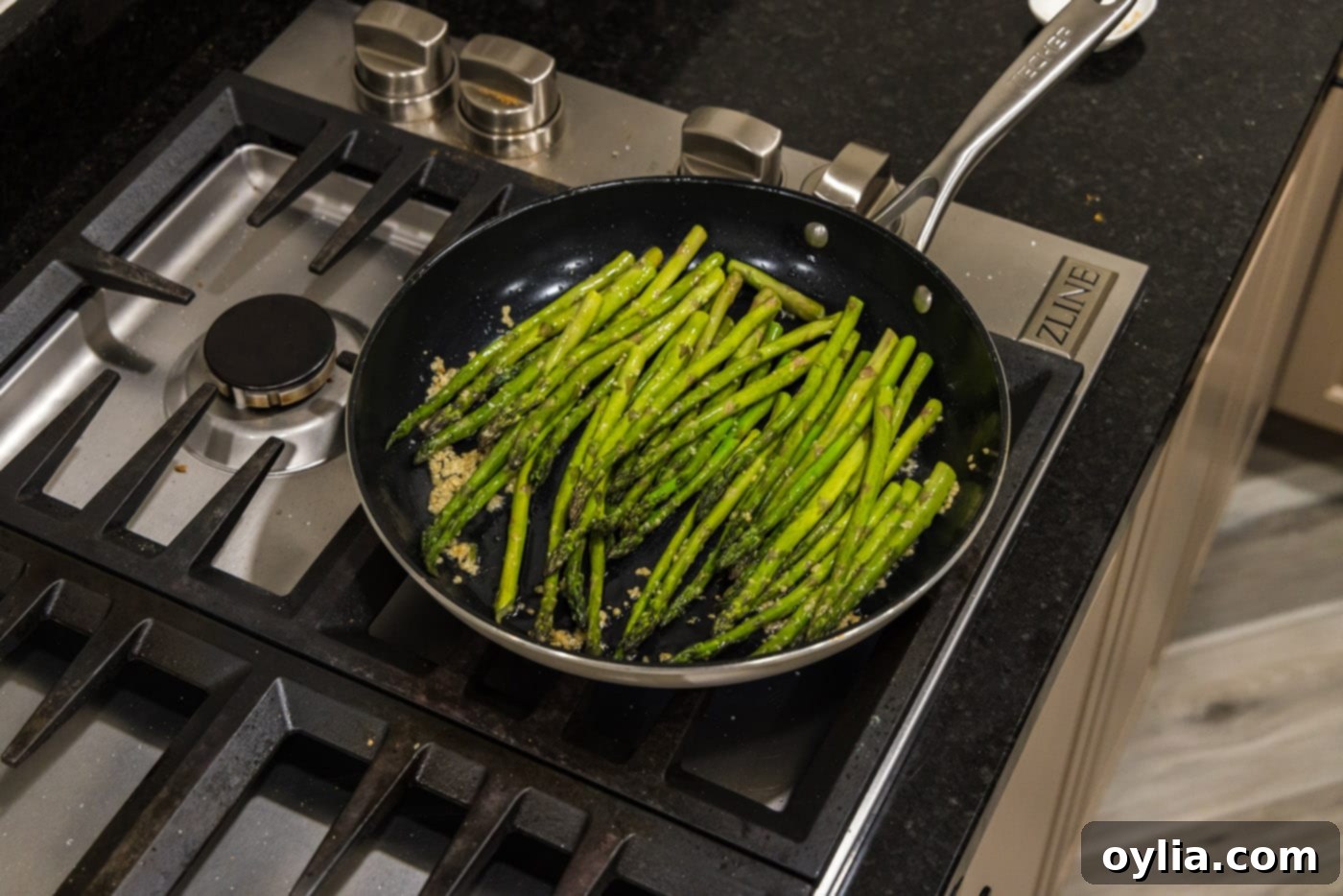 Fresh asparagus spears being added to a skillet containing hot olive oil and sautéed garlic.