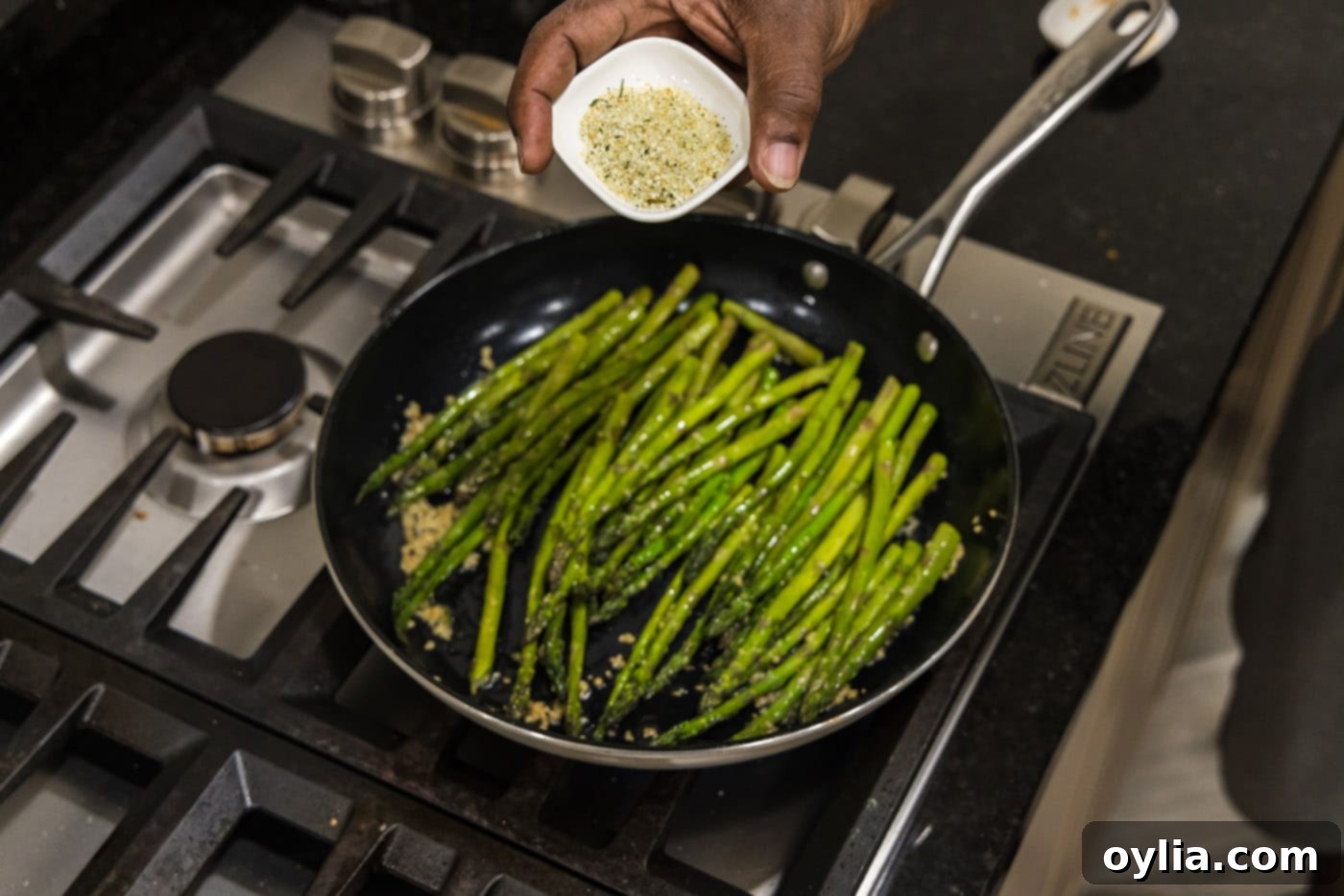 A hand sprinkling garlic salt over asparagus spears in a hot skillet.