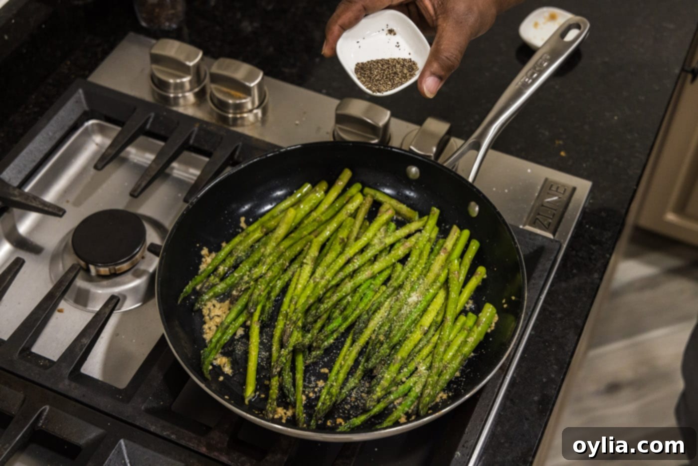 Black pepper being sprinkled over sauteing asparagus in a pan.