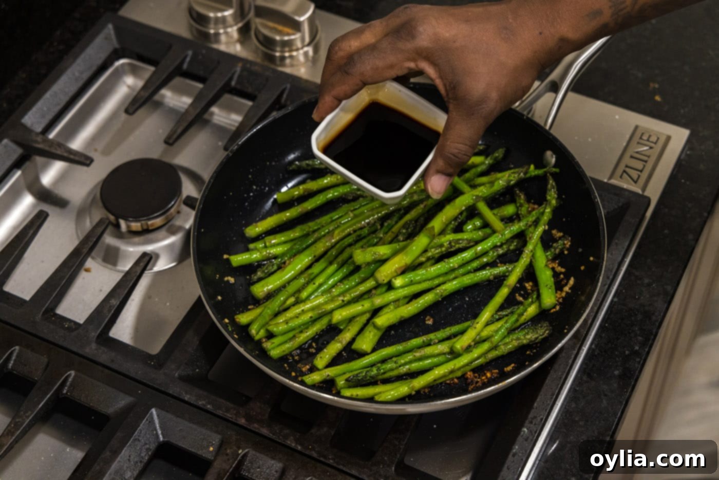 Soy sauce being poured into a skillet with sauteed asparagus and garlic.