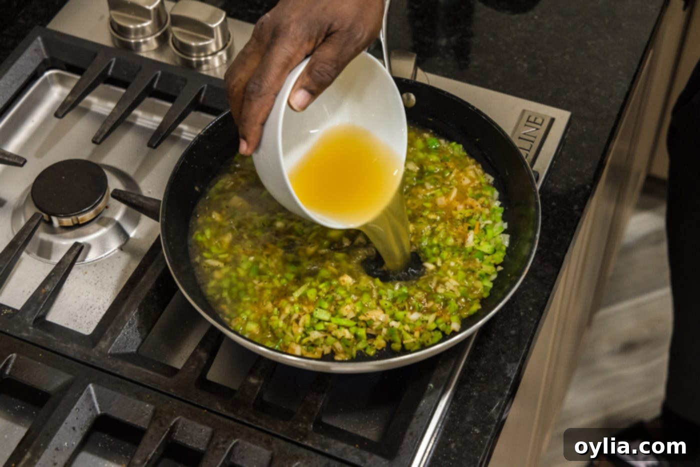 pouring chicken stock into skillet with celery, green pepper, and onion