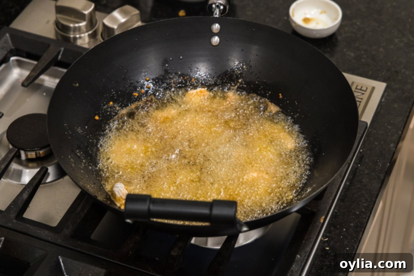 Shrimp frying in hot oil in a wok, bubbling gently.