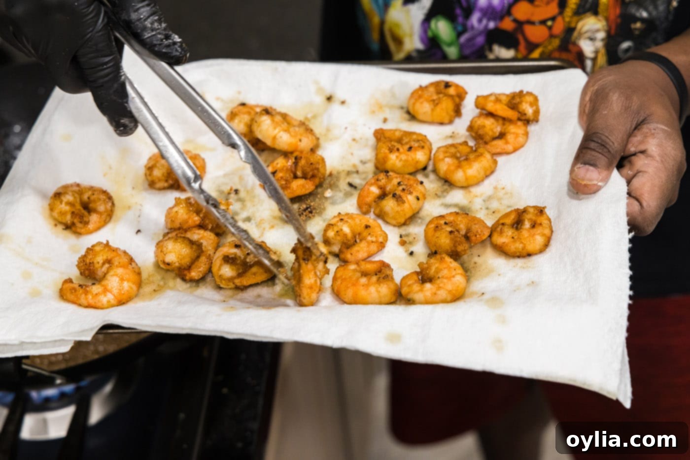 Tongs transferring fried shrimp to paper towels to drain.