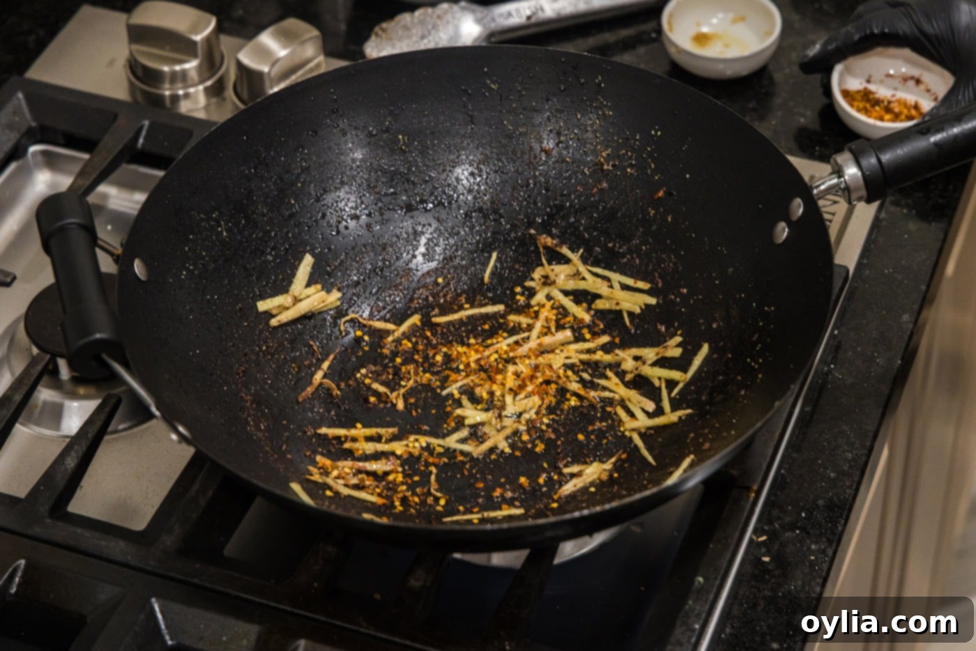 Red pepper flakes and slivered ginger in a wok, stir-frying.