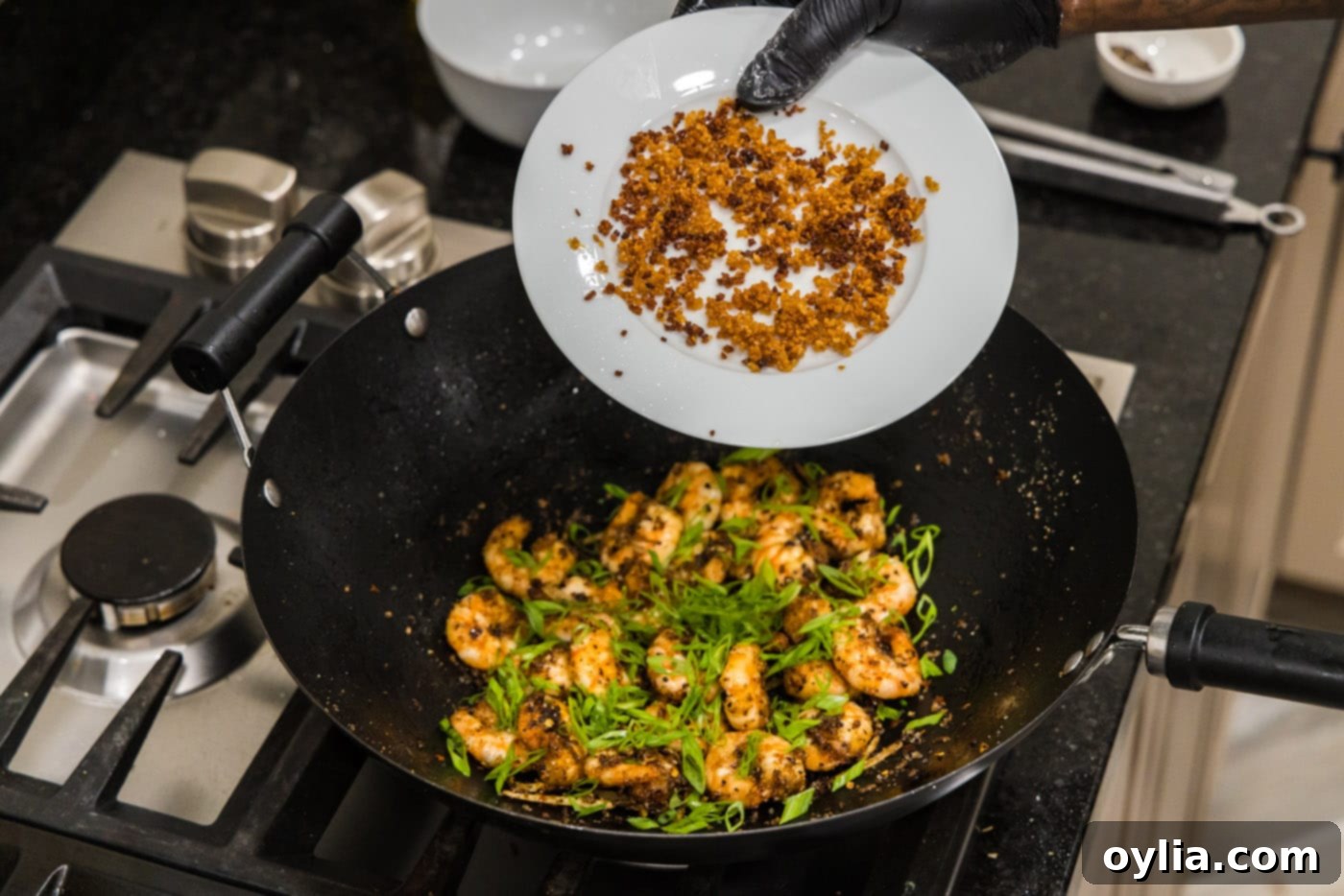 Adding fried garlic to the wok with salt and pepper shrimp, along with green onions.