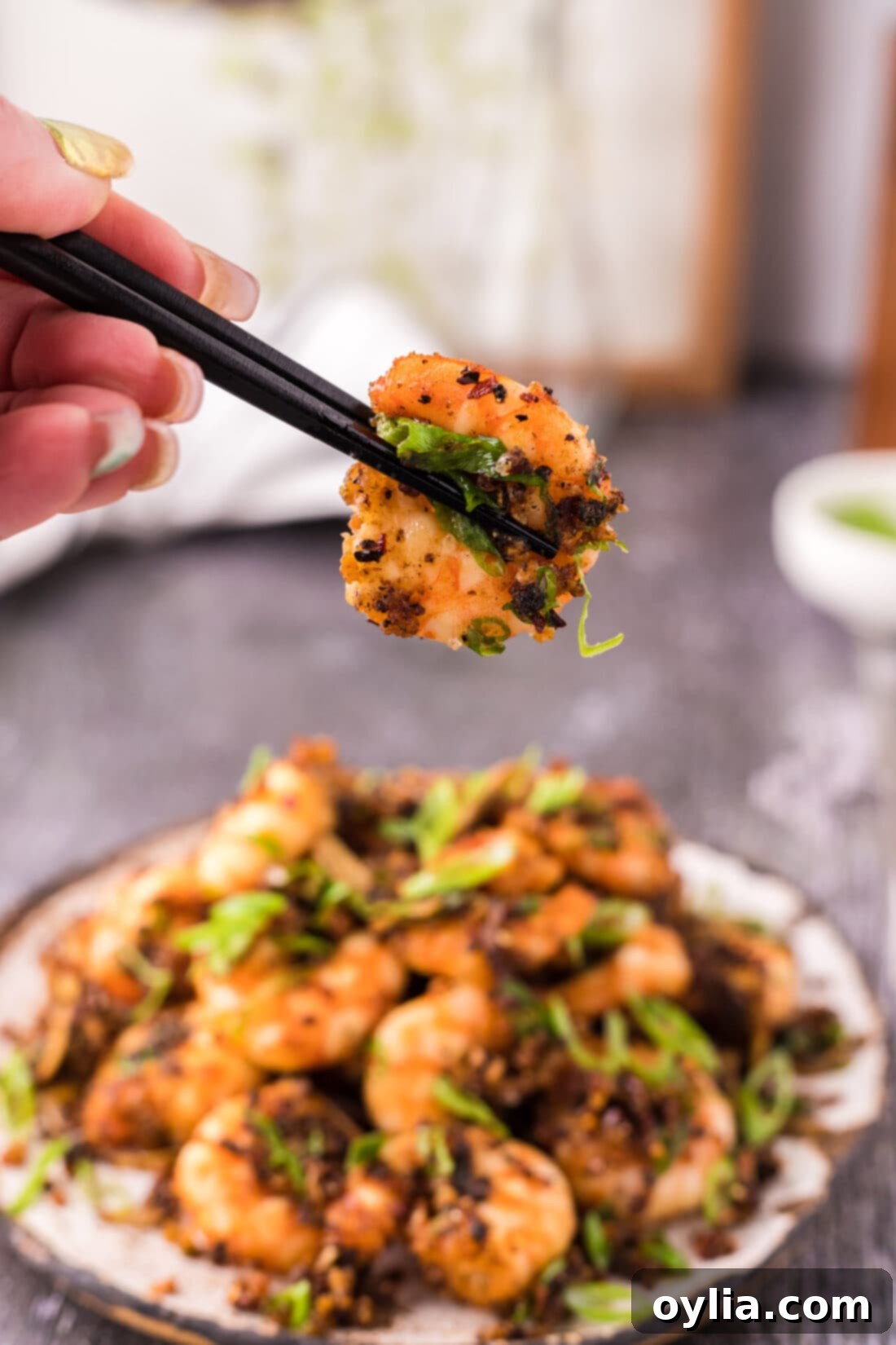 Chopsticks holding a crispy Salt and Pepper Shrimp, ready to be enjoyed.