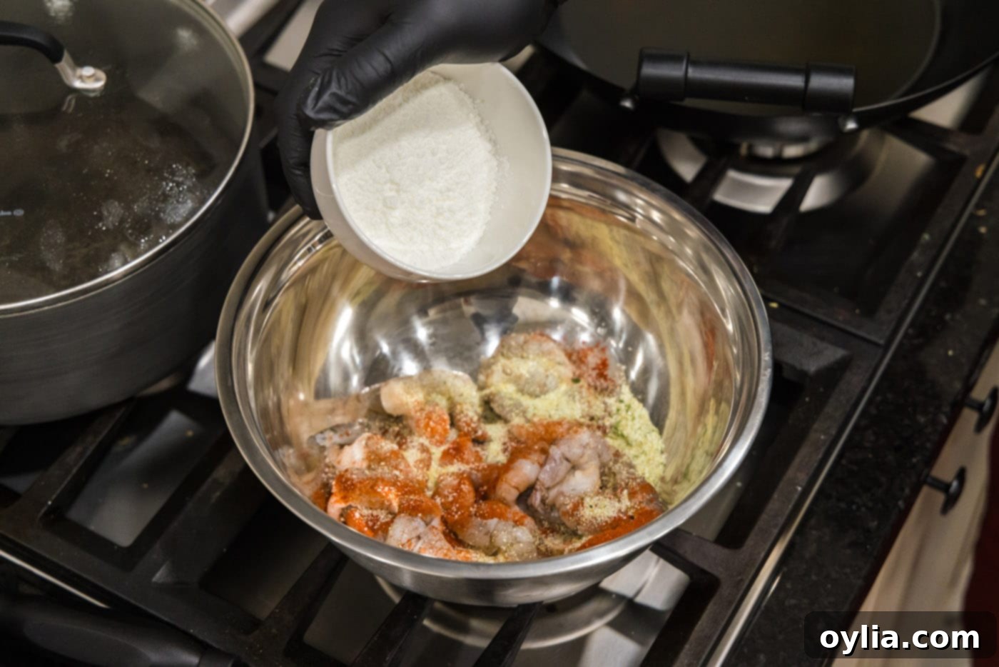Adding cornstarch to seasoned shrimp in a bowl, showing a white powder coating.