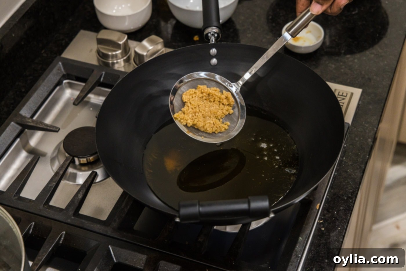 Adding minced garlic to hot oil in a wok, showing the sizzling action.