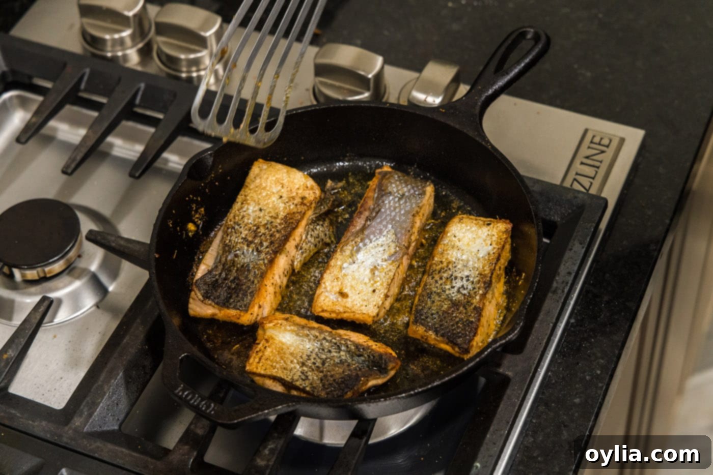 Salmon fillets cooking skin-side up in the skillet, with a beautiful golden crust visible