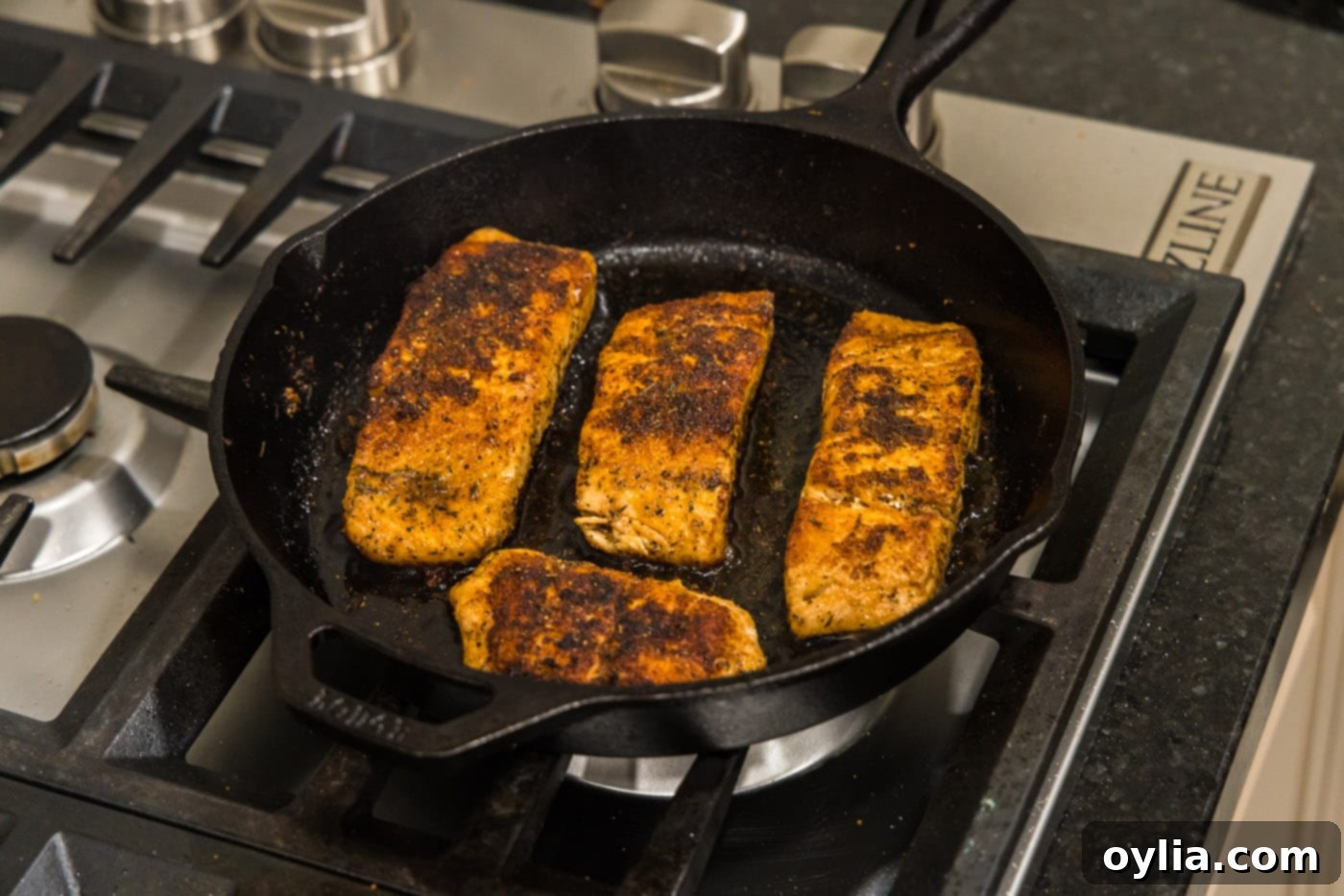 Three perfectly cooked Cajun salmon fillets resting in a hot skillet, ready to be served