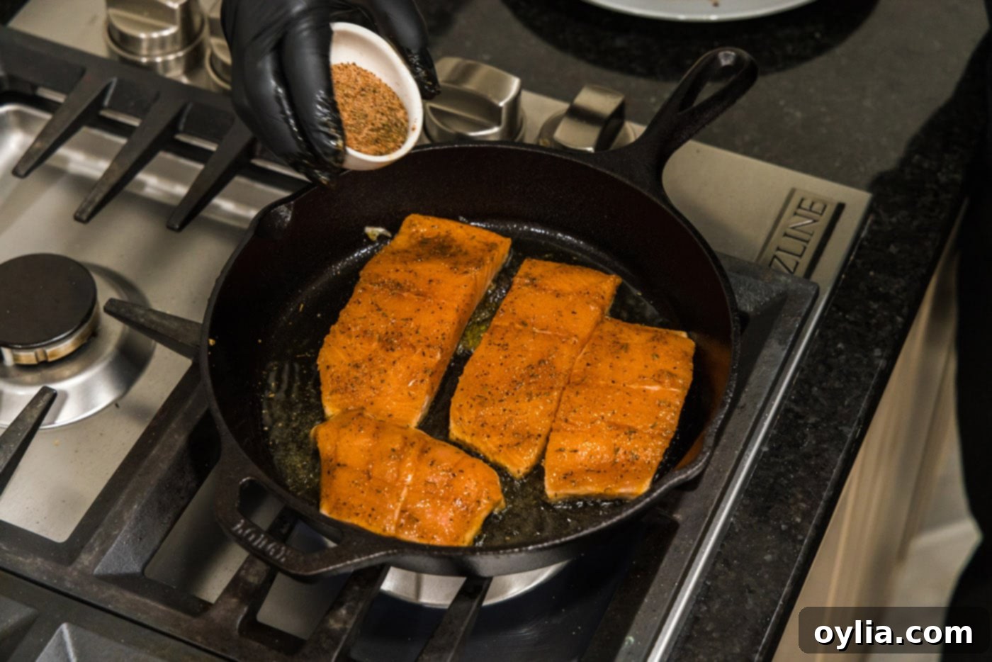 Hand sprinkling additional Cajun seasoning onto salmon fillets in a skillet