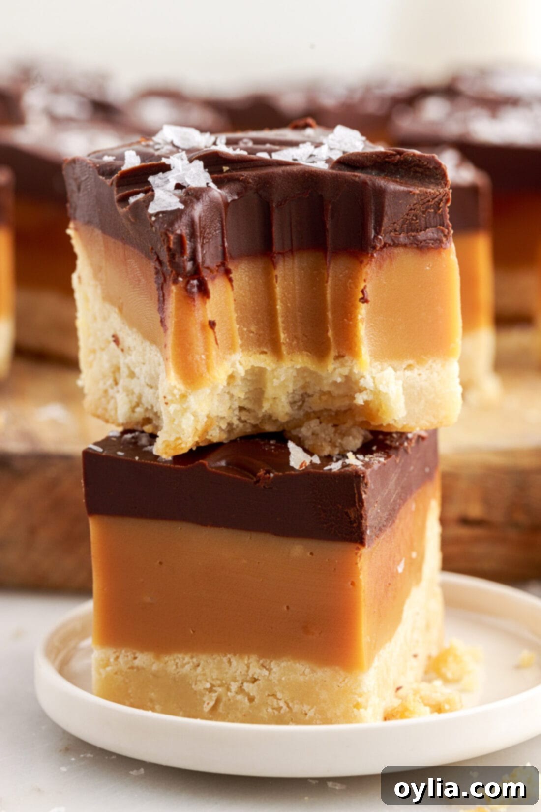 Millionaires Bars 2 Two Millionaire’s Bars stacked on top of each other with a bite taken out of the top bar, showcasing the three distinct layers: golden shortbread, amber caramel, and dark chocolate ganache.