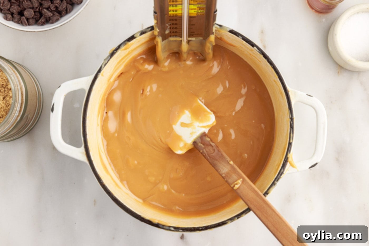A candy thermometer immersed in the simmering caramel mixture to monitor temperature.