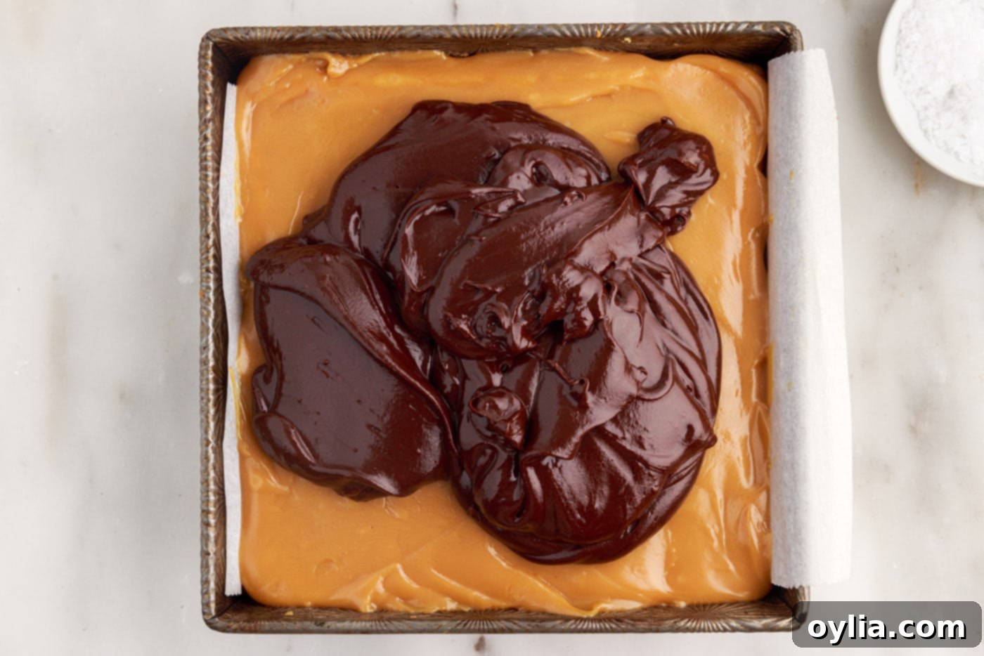 Smooth chocolate ganache being poured over the set caramel layer in the pan.