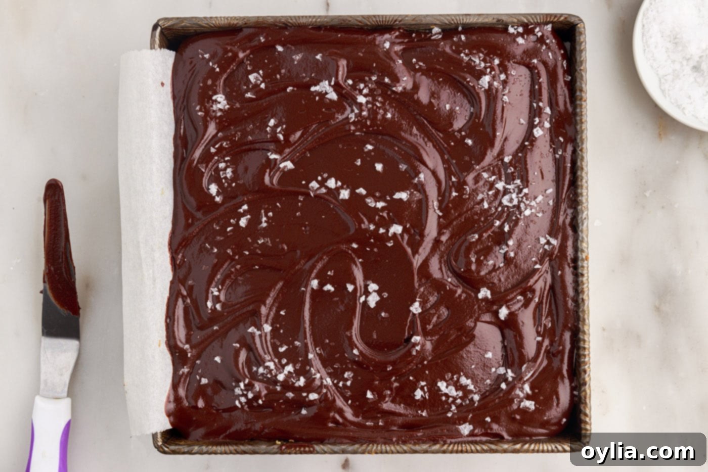 Millionaire’s bars in the pan, topped with glossy chocolate ganache and a sprinkle of flaky sea salt.